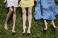 Legs of three teen girls lying on the grass - Ellery Chua