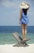 young woman standing on chair looking at ocean - Nugene Chiang