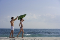 man holding giant leaf over woman as they walk on beach - Alex Mares-Manton