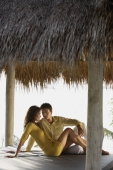 young couple sitting under thatch cabana - Alex Mares-Manton