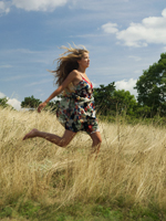 Young woman running in grassy field - Alex Hajdu