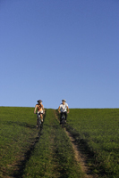 Young couple riding bicycles down hillside - Alex Mares-Manton