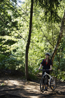 Young woman pushing mountain bike through forest - Alex Mares-Manton