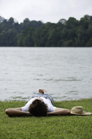 Young man lying on grass near lake - Nugene Chiang