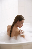 Young woman in bath tub, scrubbing shoulder - Alex Mares-Manton