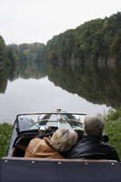 Senior couple sitting in antique car, looking out at pond - Alex Mares-Manton