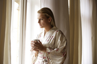 Young woman standing with coffee cup by window - Alex Mares-Manton
