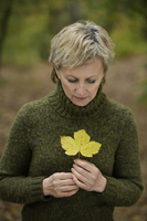 Senior woman holding autumn leaf - Alex Mares-Manton