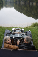 senior couple sitting near pond in antique car - Alex Mares-Manton