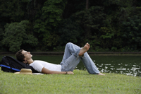 Young man resting on grass near lake - Nugene Chiang