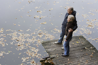 Senior couple standing on wooden pier looking at pond - Alex Mares-Manton