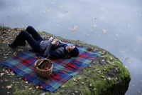 Young woman lying on blanket near lake - Alex Mares-Manton