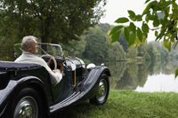 Senior man looking at lake from antique car - Alex Mares-Manton