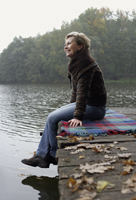 Senior woman sitting on pier looking at pond - Alex Mares-Manton