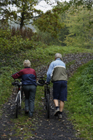 Senior couple pushing bikes up hill - Alex Mares-Manton