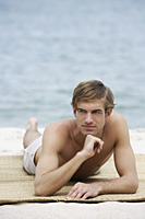 young man resting on beach mat - Alex Mares-Manton