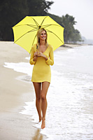 woman walking on beach with yellow umbrella - Nugene Chiang