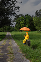young boy sitting on roadside with orange umbrella - Nugene Chiang