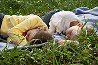 brother and sister lying on blanket in park - Nugene Chiang