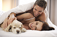 Young couple playing with puppy in bed - Alex Mares-Manton