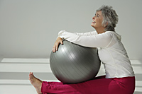 Mature woman holding exercise ball, looking up. - Nugene Chiang