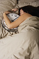 woman sleeping in bed holding a large clock - Nugene Chiang