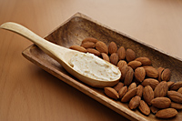 Almonds and almond scrub in wooden spoon. - Nugene Chiang