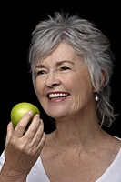 Older woman smiling holding an apple. - Nugene Chiang