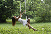 Woman in white dress swinging in tree swing. - Nugene Chiang