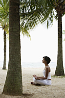 Young woman doing yoga on beach, under coconut trees, meditating. - Alex Mares-Manton