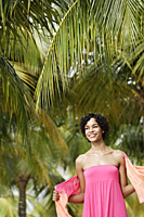 young woman under green coconut trees, smiling. - Alex Mares-Manton
