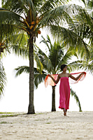woman walking on beach under coconut trees wearing pink. - Alex Mares-Manton