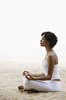 woman sitting on beach doing yoga, eyes closed. - Alex Mares-Manton