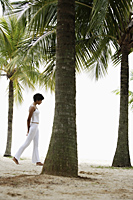 Woman walking under coconut trees on beach. - Alex Mares-Manton