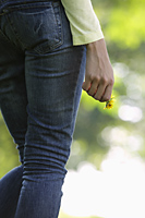 back view of woman wearing jeans and holding yellow flower - Alex Mares-Manton