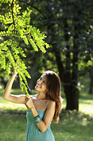 young woman looking at leaves of tree and smiling - Alex Mares-Manton
