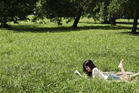 woman laying on her stomach on grass reading a book - Alex Mares-Manton