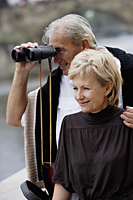 mature man looking through binoculars with woman looking at view - Alex Hajdu