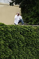mature man standing on top of a ivy covered wall taking a photo - Alex Hajdu
