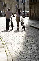 young couple walking bikes down cobbled street - Alex Hajdu