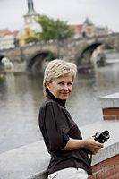 mature woman standing near bridge holding binoculars - Alex Hajdu