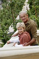 mature couple standing on balcony smiling with trees in background - Alex Hajdu