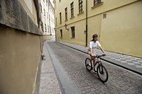 young woman riding bicycle down cobblestone street - Alex Hajdu