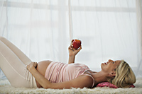 pregnant woman laying on back holding apple - Alex Mares-Manton