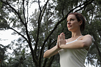Young woman holding hands together in yoga pose under trees - Alex Mares-Manton