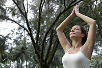 Young woman holding hands up in yoga pose under trees - Alex Mares-Manton