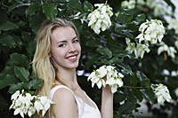 Young blonde woman standing in front of white flowers - Alex Mares-Manton